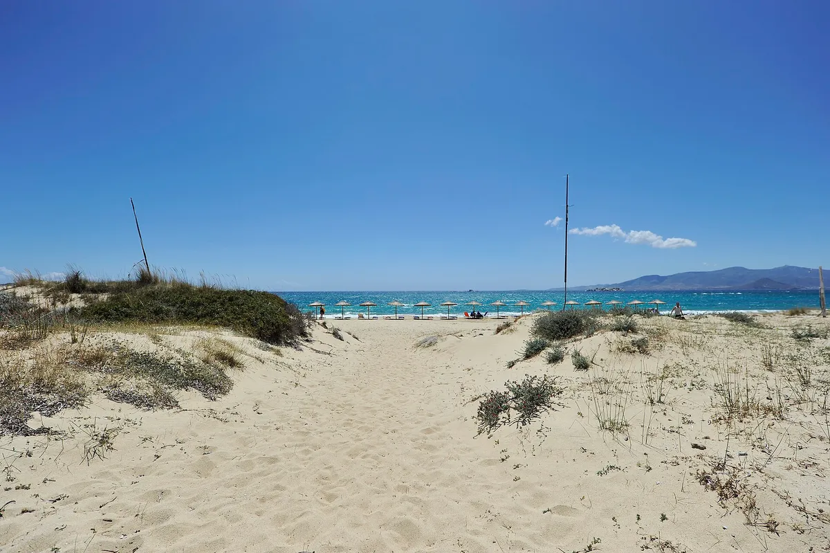 Sandy path through dunes to Plaka beach with umbrellas on the west coast of Naxos, Greece