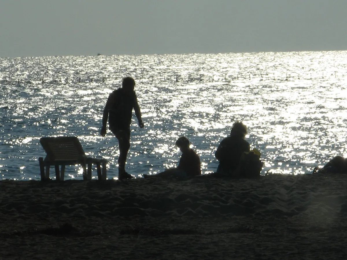 Family silhouetted on a beach at dusk with the sea glittering behind