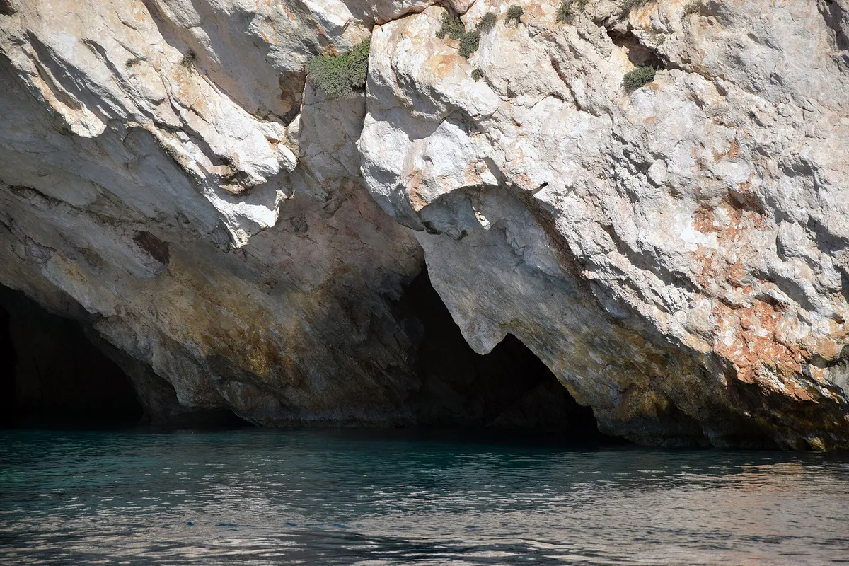 Limestone sea-cave walls meeting still green water inside a cavern on a Greek island coast