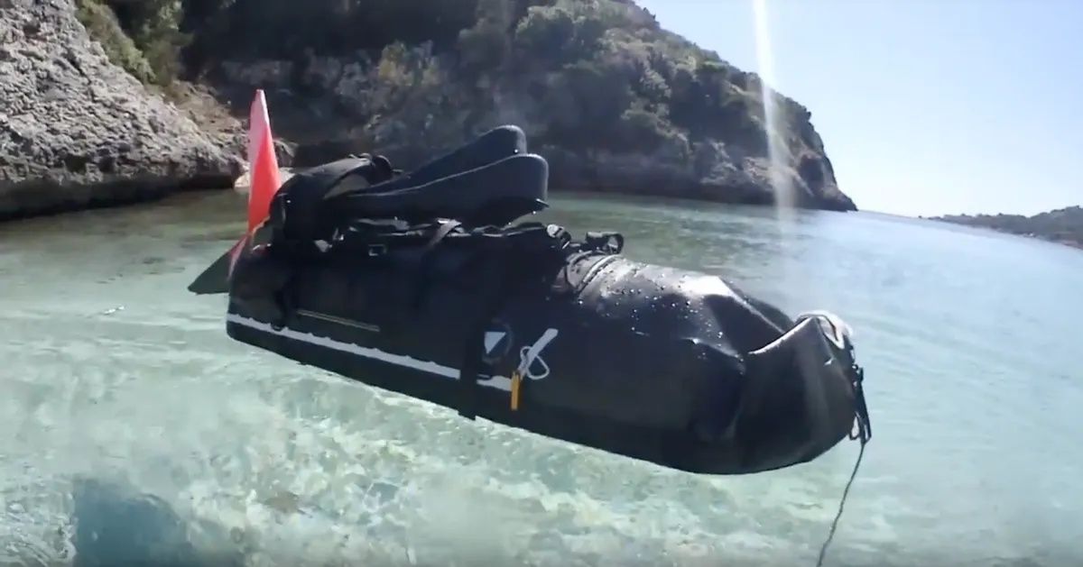 Black waterproof dry bag floating in clear shallow water inside a rocky cove